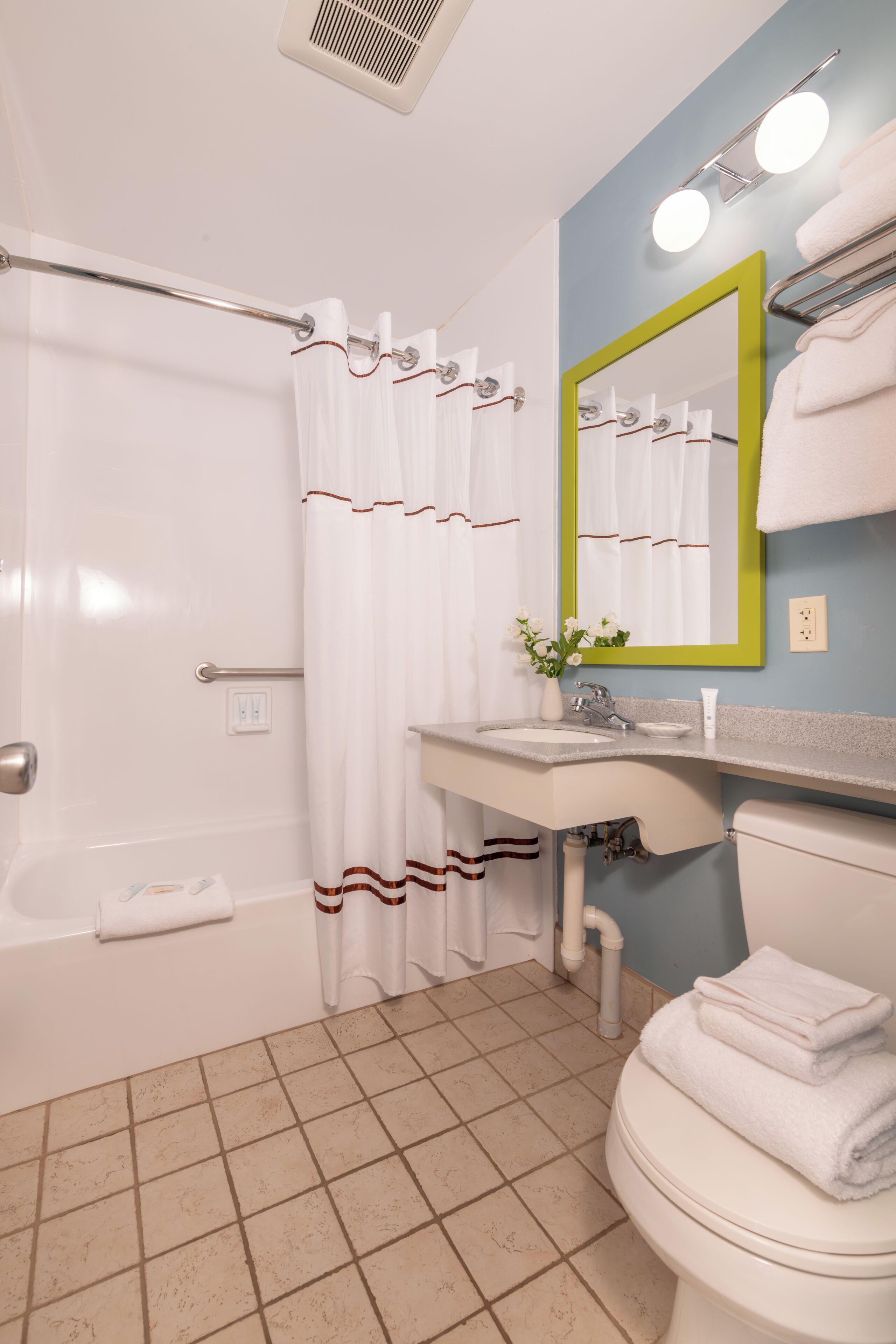 A bathroom with a bathtub, toilet, sink, and a mirror with a green frame.