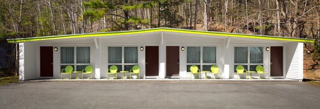 A single-story motel with a covered front porch, a row of single chairs, and a parking area.