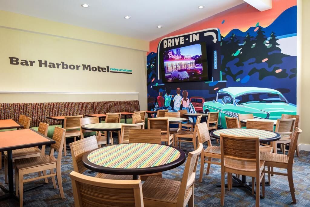 A Bar Harbor Motel restaurant with booths and round tables, a mural of a car and people, and a neon sign.