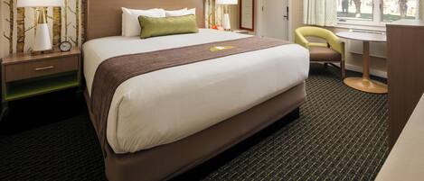A hotel room with a large bed, a desk, a chair, and a window with a view of trees.