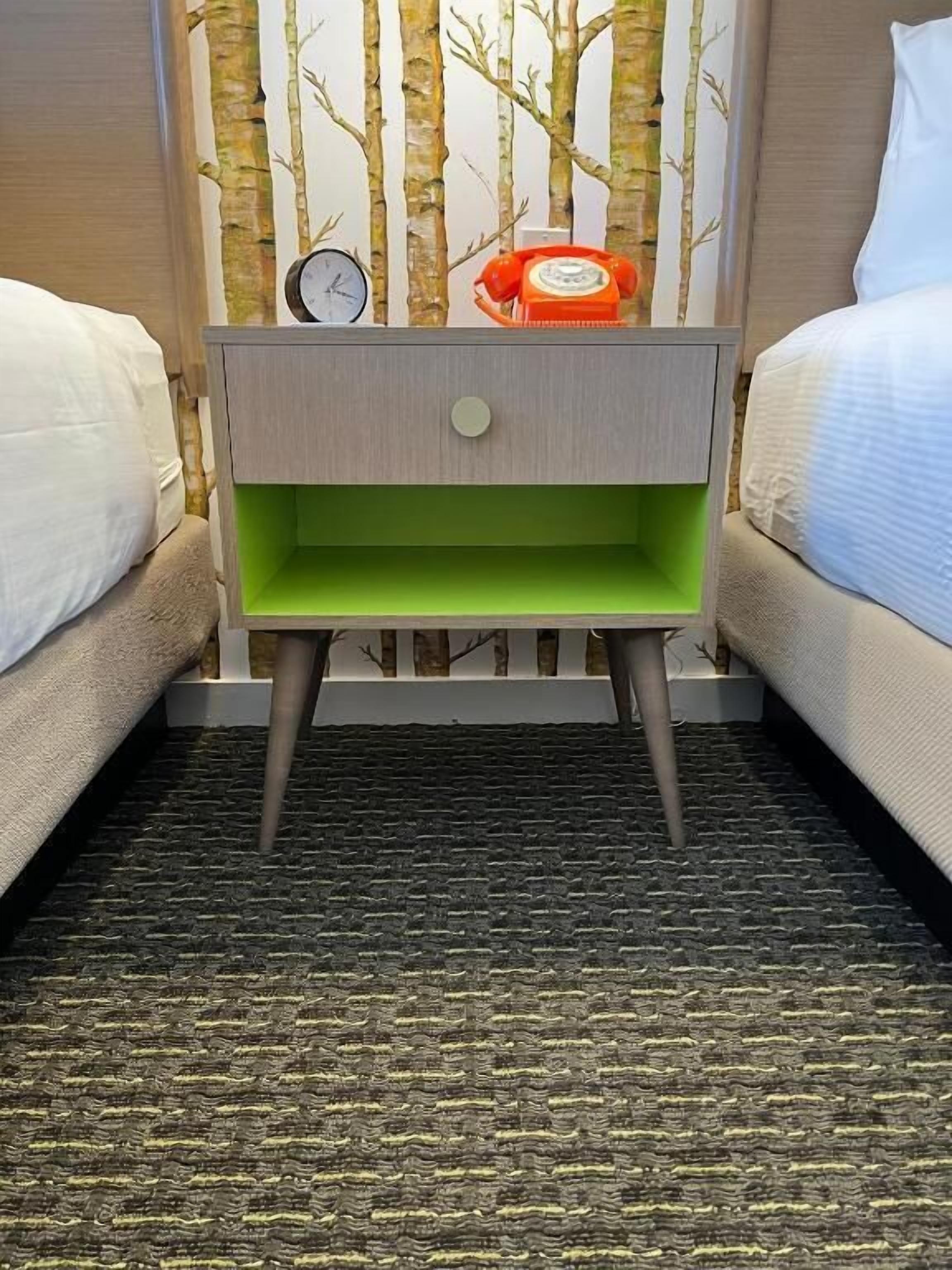 Una habitación de hotel con una mesita de noche verde, un reloj y un teléfono rojo.