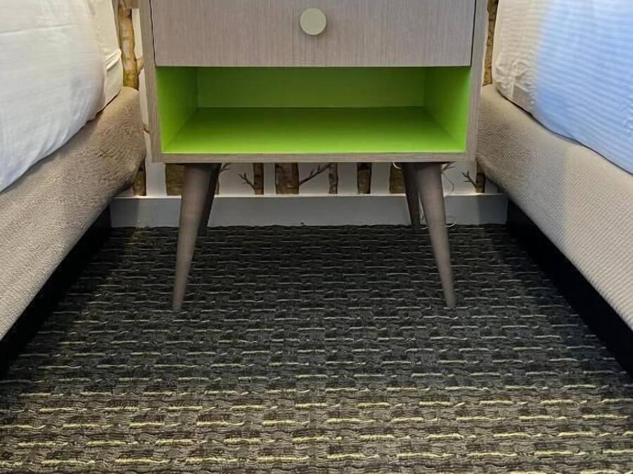 Una habitación de hotel con una mesita de noche verde, un reloj y un teléfono rojo.