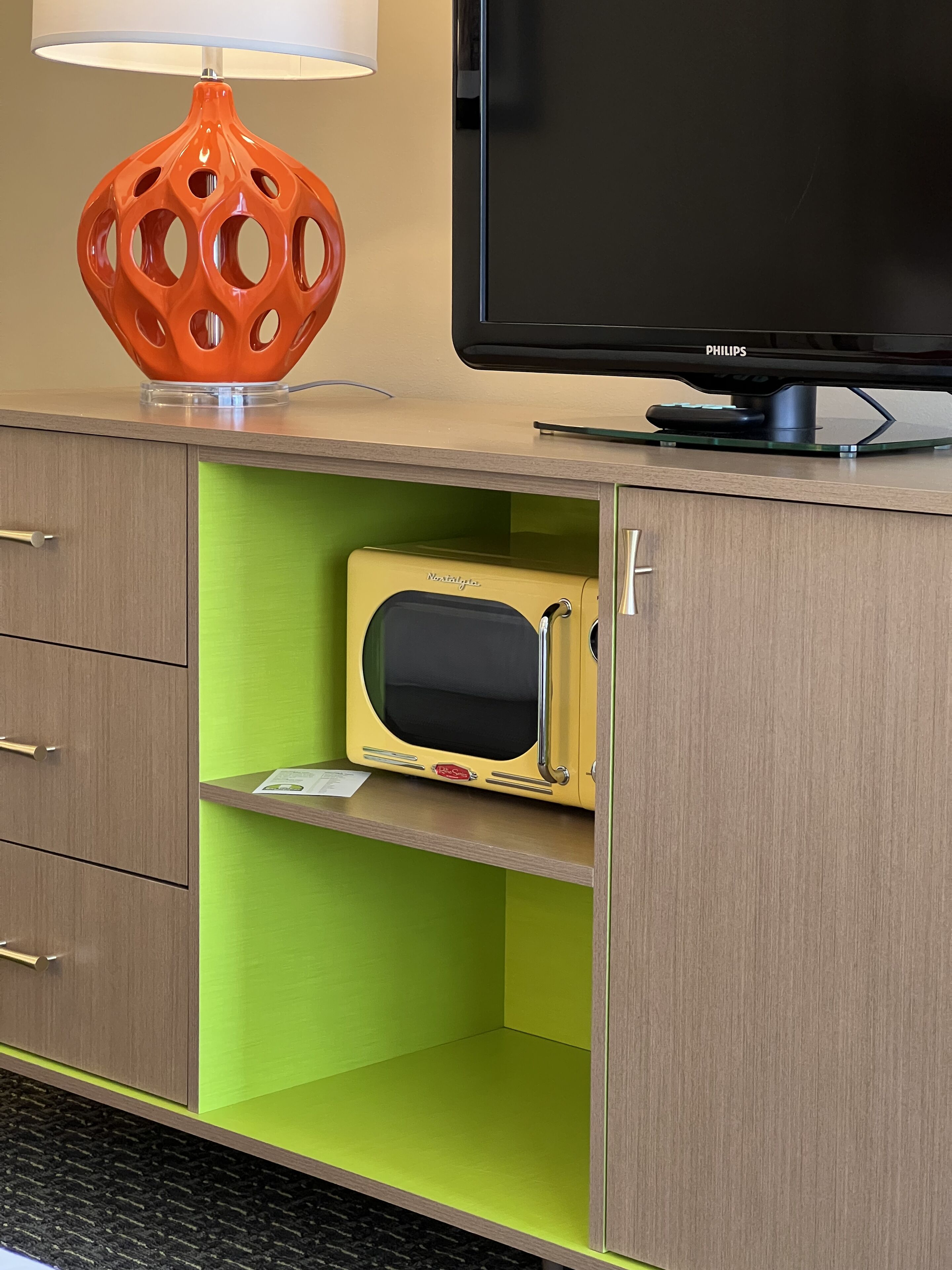 A modern hotel room with a flat-screen TV, a retro-style microwave, and a unique orange lamp.