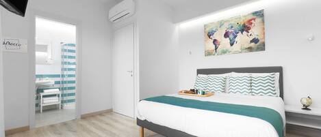 Une chambre à coucher moderne avec un lit, une œuvre d’art représentant une carte du monde et une salle de bain visible à travers une porte ouverte.