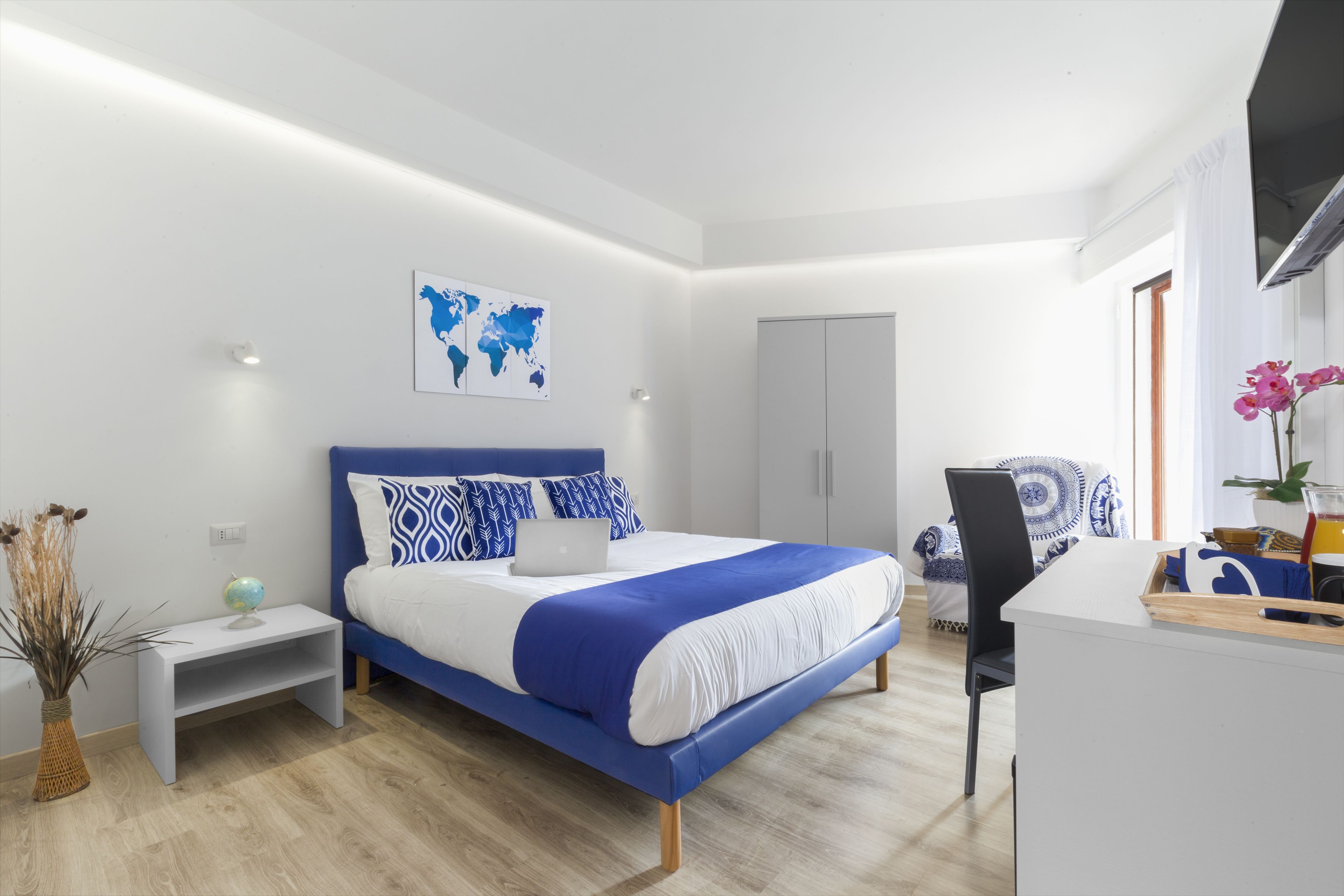Een moderne slaapkamer met een bed, een bureau en een stoel. Er staat een wereldbol op het nachtkastje en een plant op het bureau.