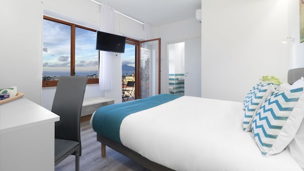 A hotel room with a bed, a desk, a chair, a TV, and a window with a view.