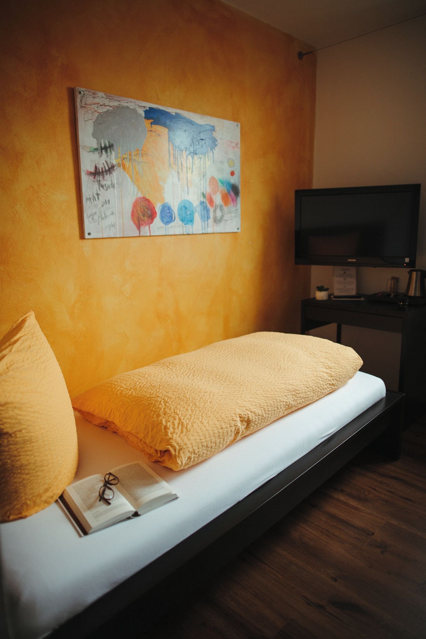 Een slaapkamer met een bed, een schilderij, een televisie en een bureau.