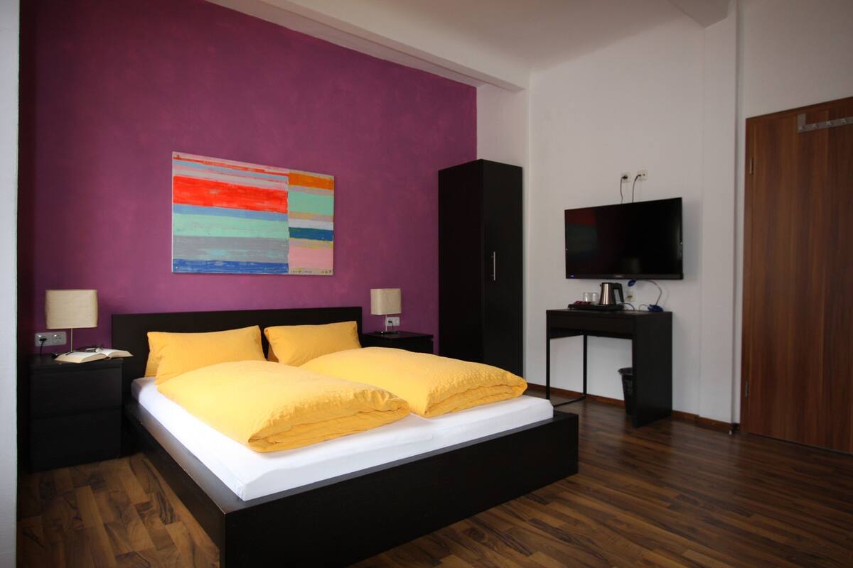 A bedroom with a bed, a television, a desk, and a wardrobe.