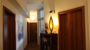 A hallway with wooden flooring, a bookshelf, a statue, and a door with a sign. - Stadthotel Kleiner Berg (Friedrichshafen)