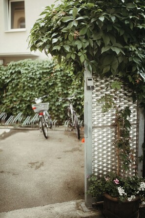 A metal gate with a plant growing over it, a bicycle parked behind, and a building in the background. - Stadthotel Kleiner Berg (Friedrichshafen)