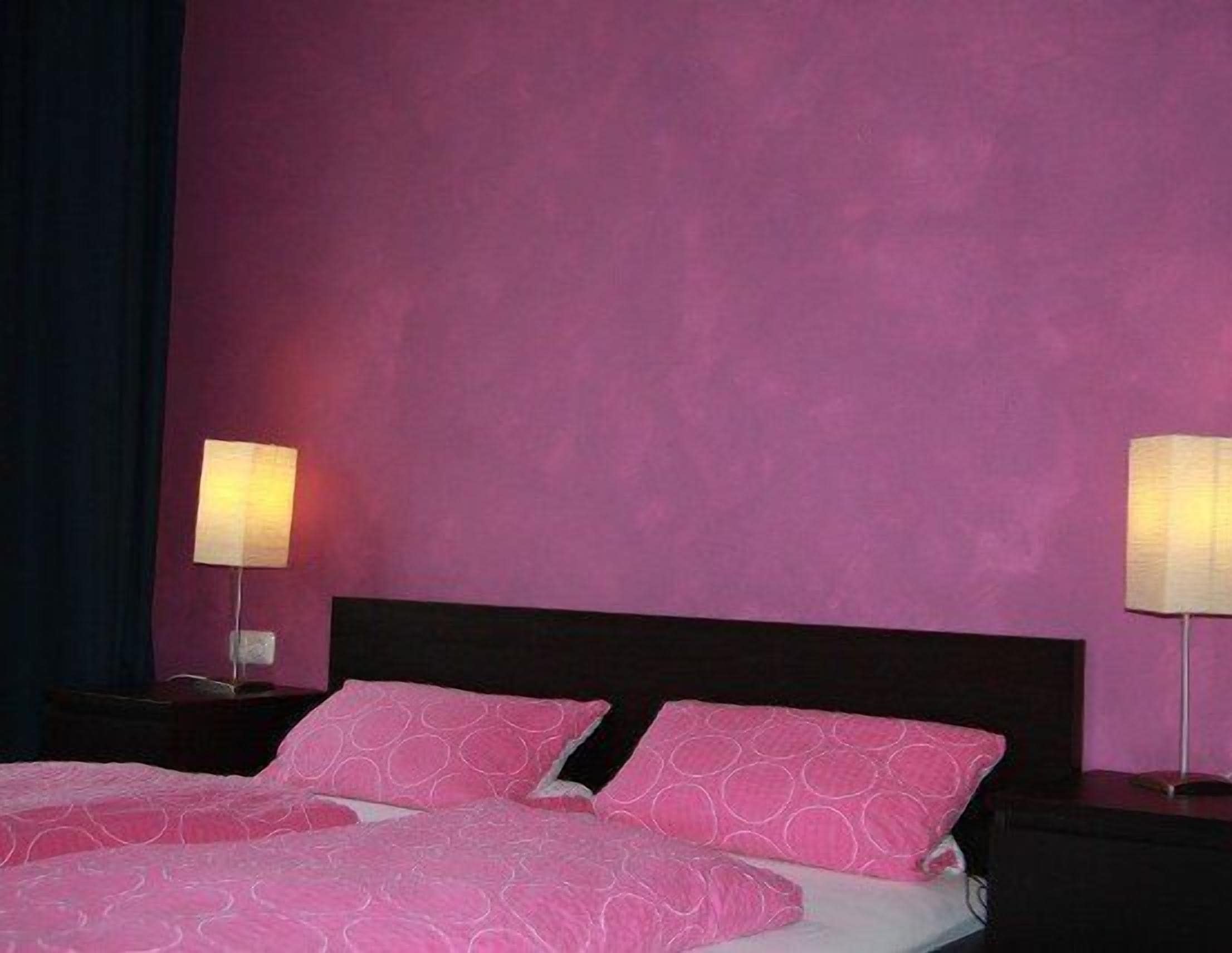 A hotel room with a bed, two bedside lamps, and a dark headboard.