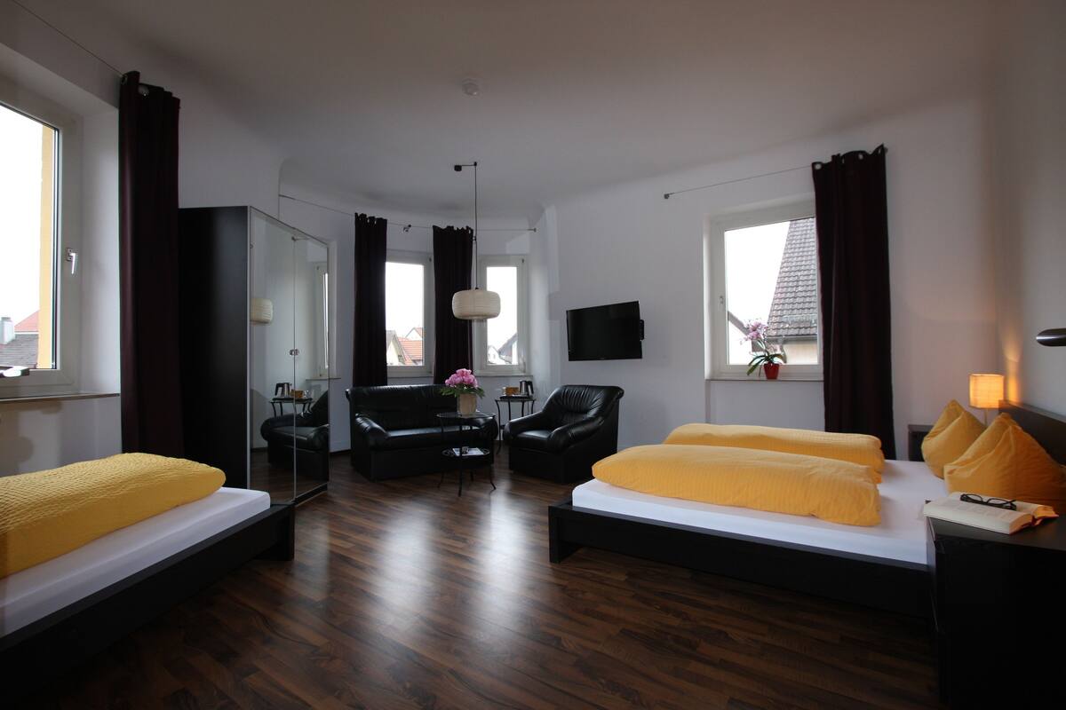 A hotel room with a bed, a sofa, a chair, a TV, and a window with curtains.
