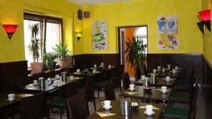 A restaurant with yellow walls, wooden tables, and green cushioned chairs. - Stadthotel Kleiner Berg (Friedrichshafen)