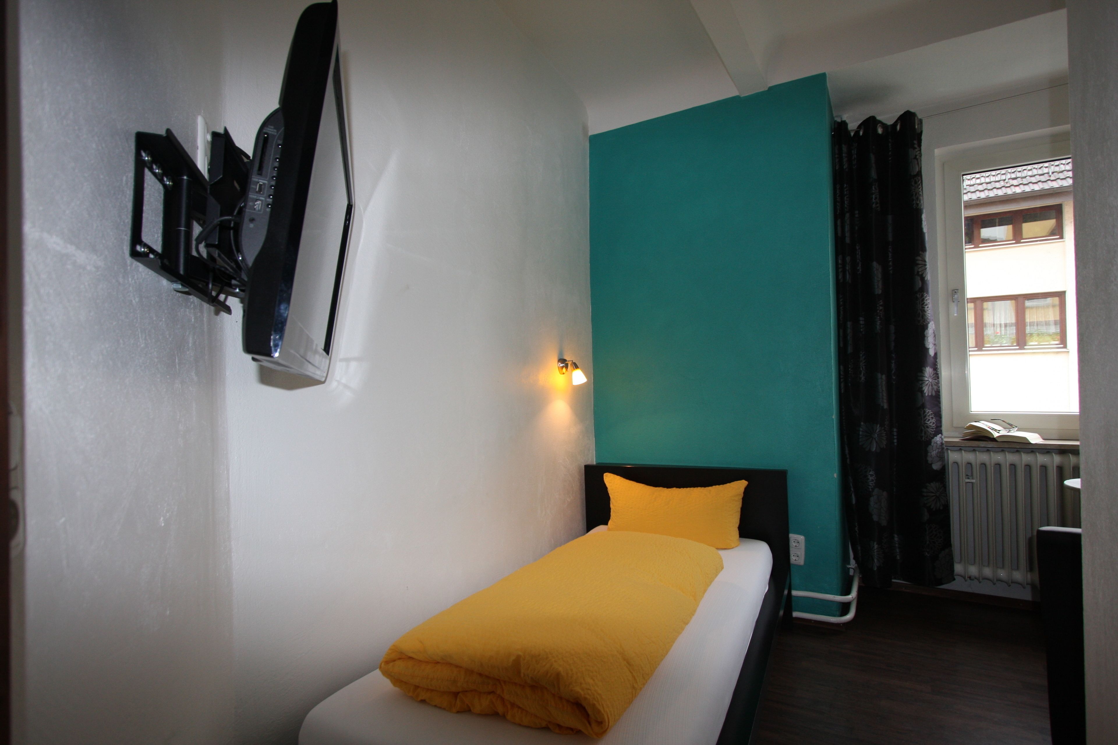 A single bed with a yellow blanket, a black headboard, and a teal accent wall.
