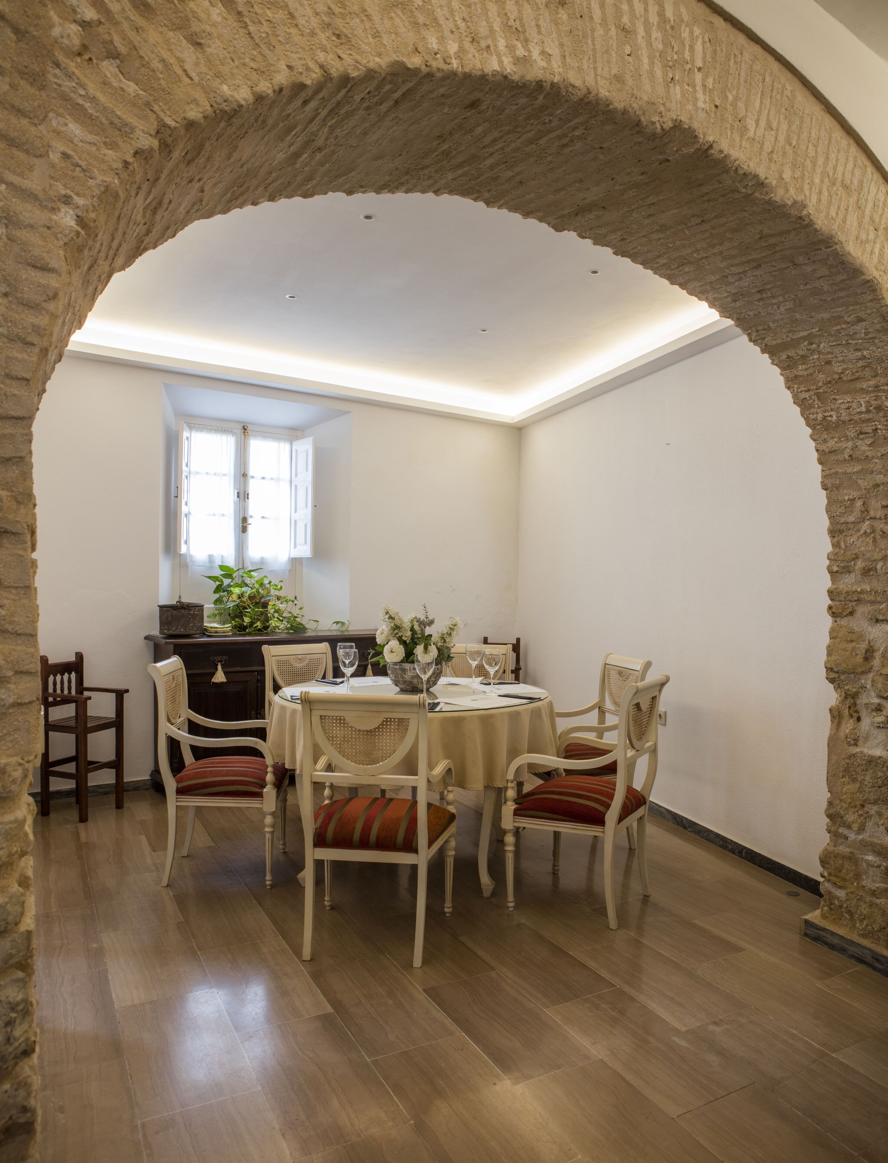 Un coin repas agrémenté d’une arche en pierre, d’une table dressée pour quatre personnes et d’une fenêtre ornée de rideaux.