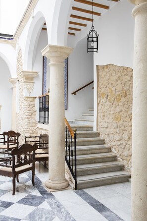 A spacious interior with a marble floor, stone walls, and wooden furniture. - TUGASA HOTEL CASA PALACIO MEDINA SIDONIA (Medina-Sidonia)