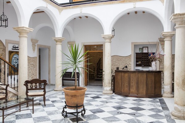A lobby with a checkered floor, a reception desk, a bench, and a potted plant.