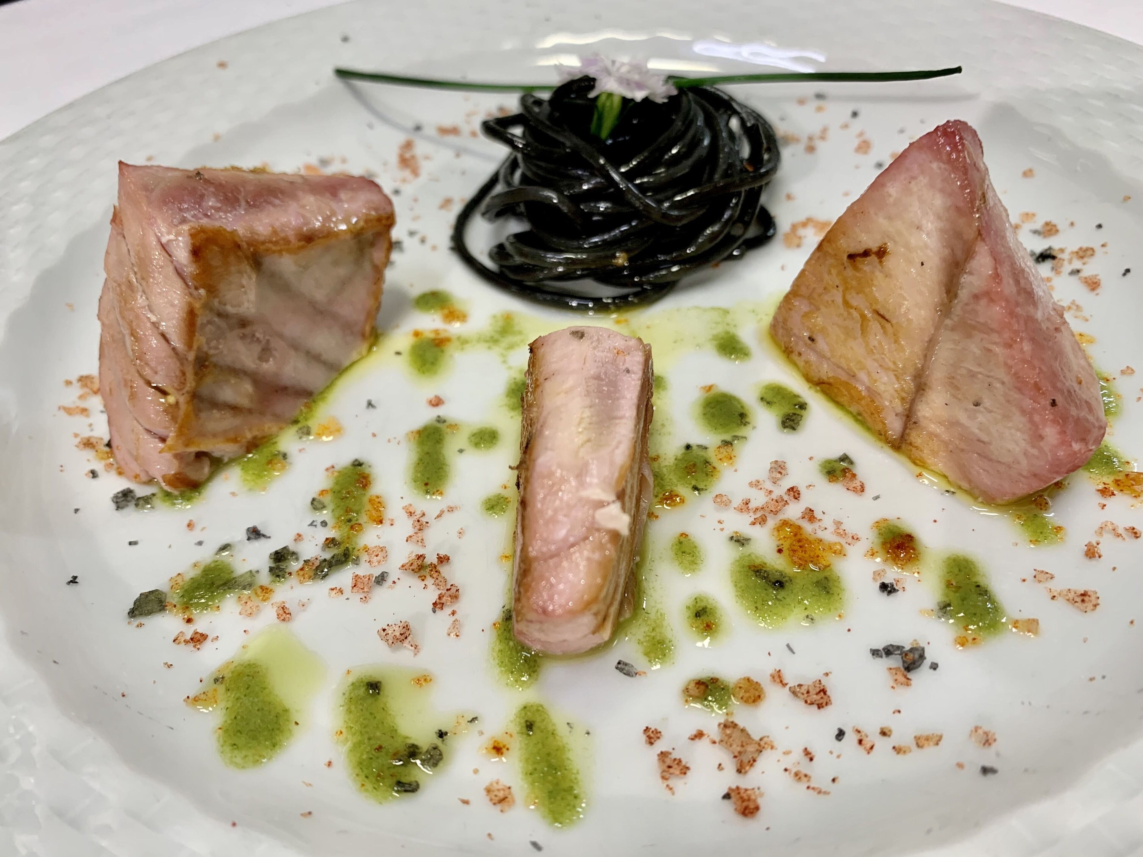 A plate with three pieces of meat and a black spiral vegetable garnish.