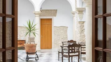 Un umbral abierto que da a un patio con suelo de cuadros, una puerta de madera, una planta en maceta y un banco.