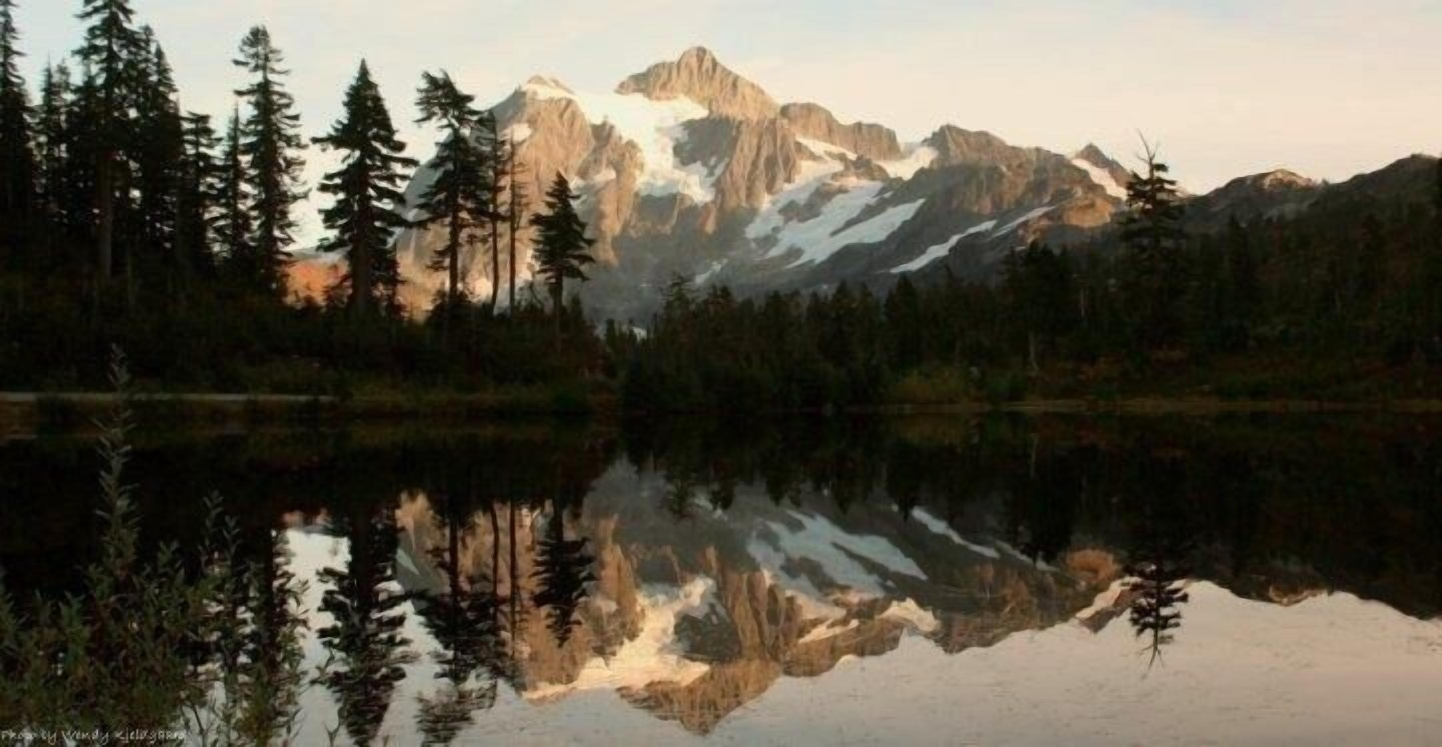 Paisaje montañoso con un lago que refleja los árboles y las cumbres.