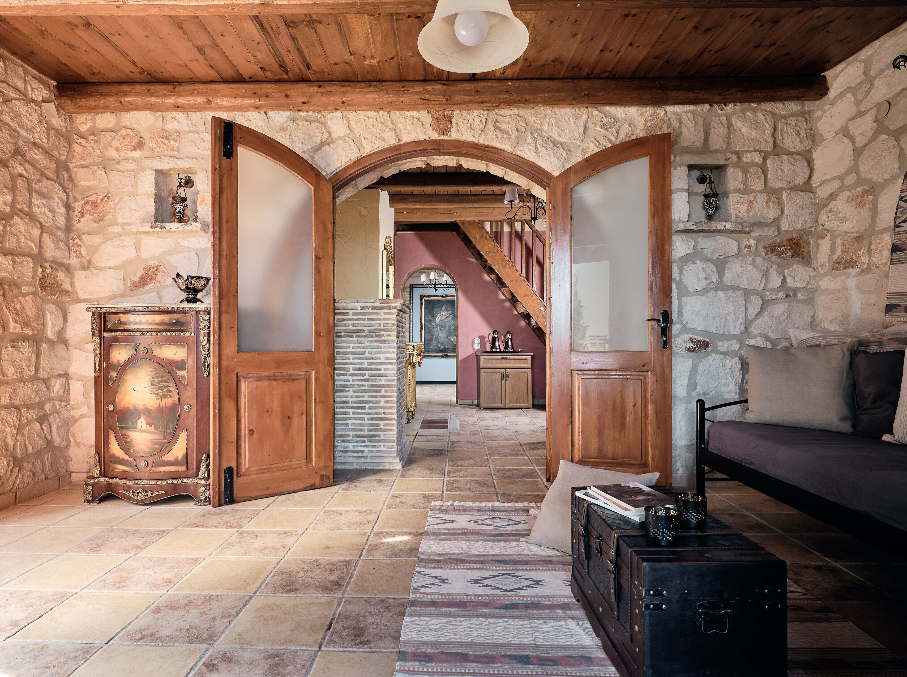 Un interior rústico con pared de piedra, puertas de madera, una escalera y una zona de estar acogedora.