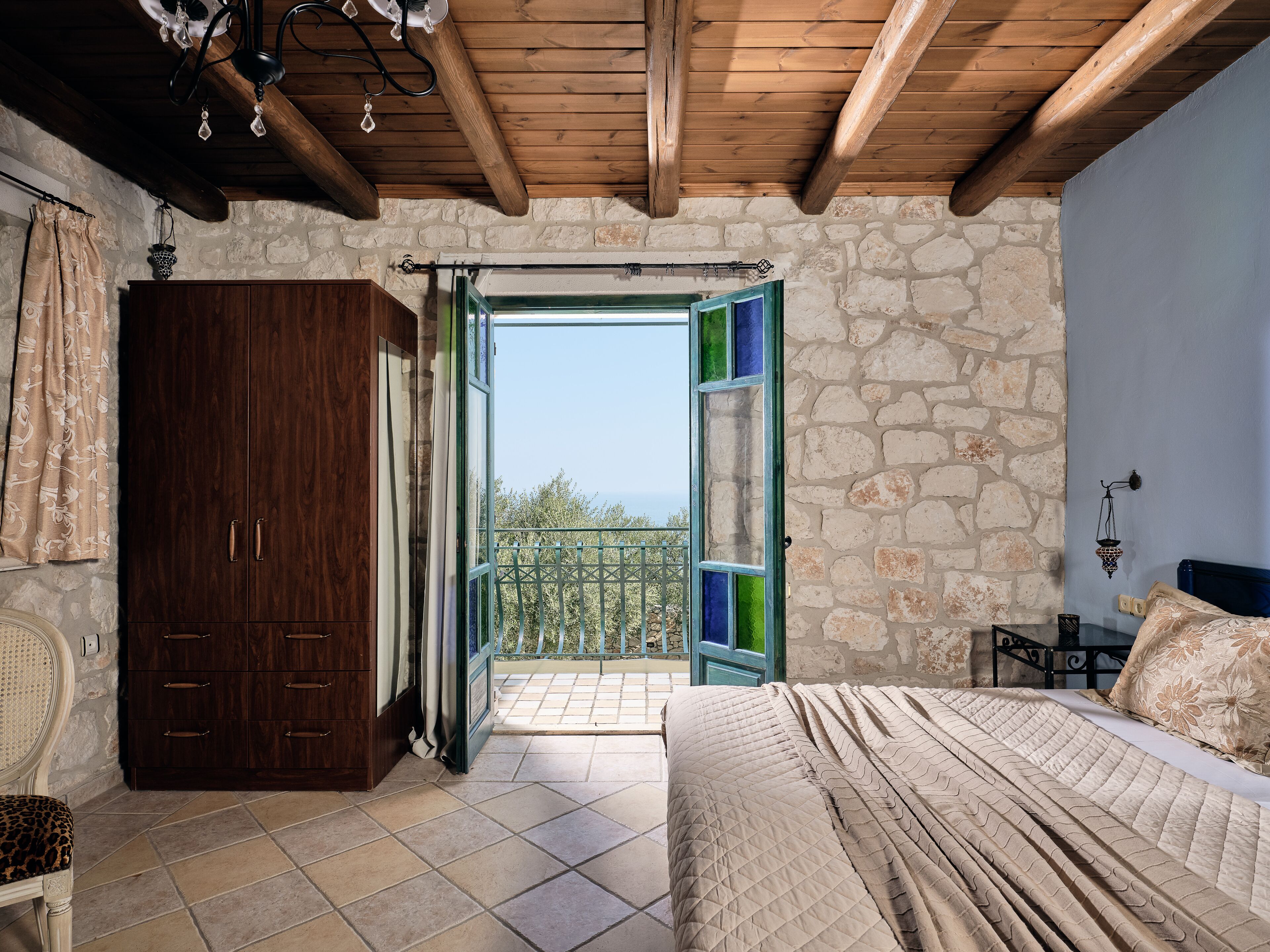 A bedroom with a large bed, a wardrobe, and a balcony with a view.