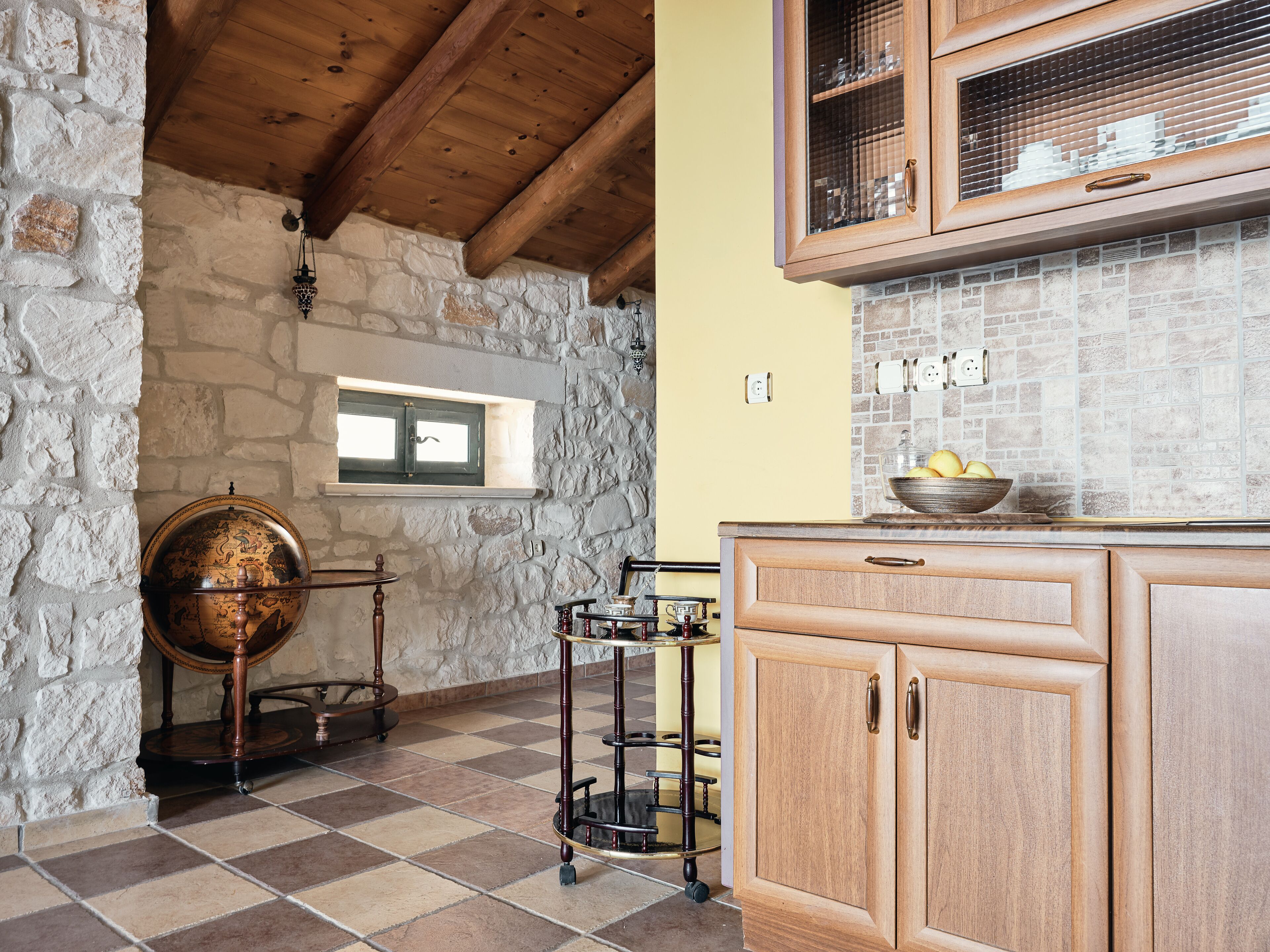 Una cocina con paredes de piedra, armarios de madera y un globo terráqueo sobre un soporte.