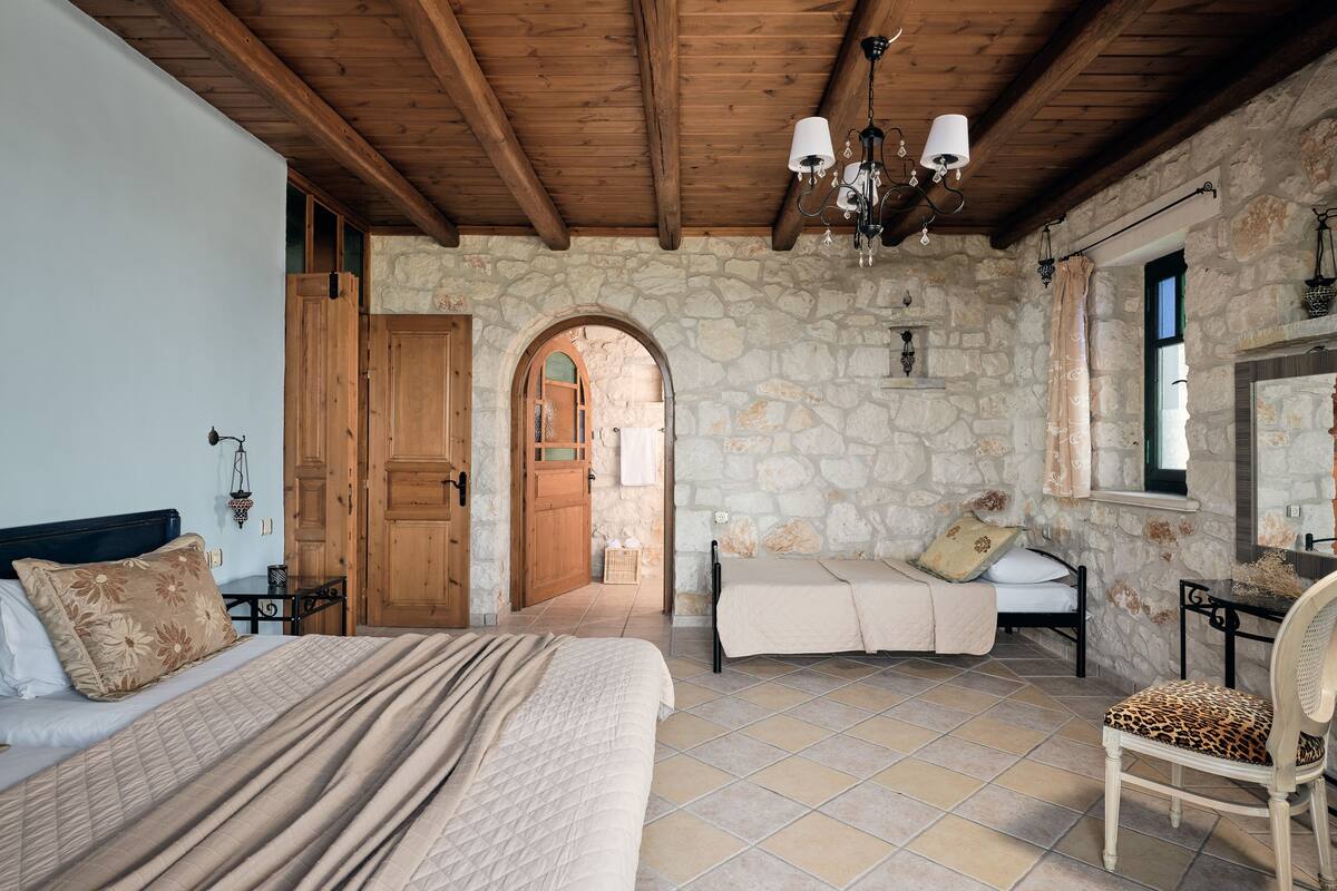 A bedroom with a large bed, a chair, a stone wall, and a wooden ceiling.