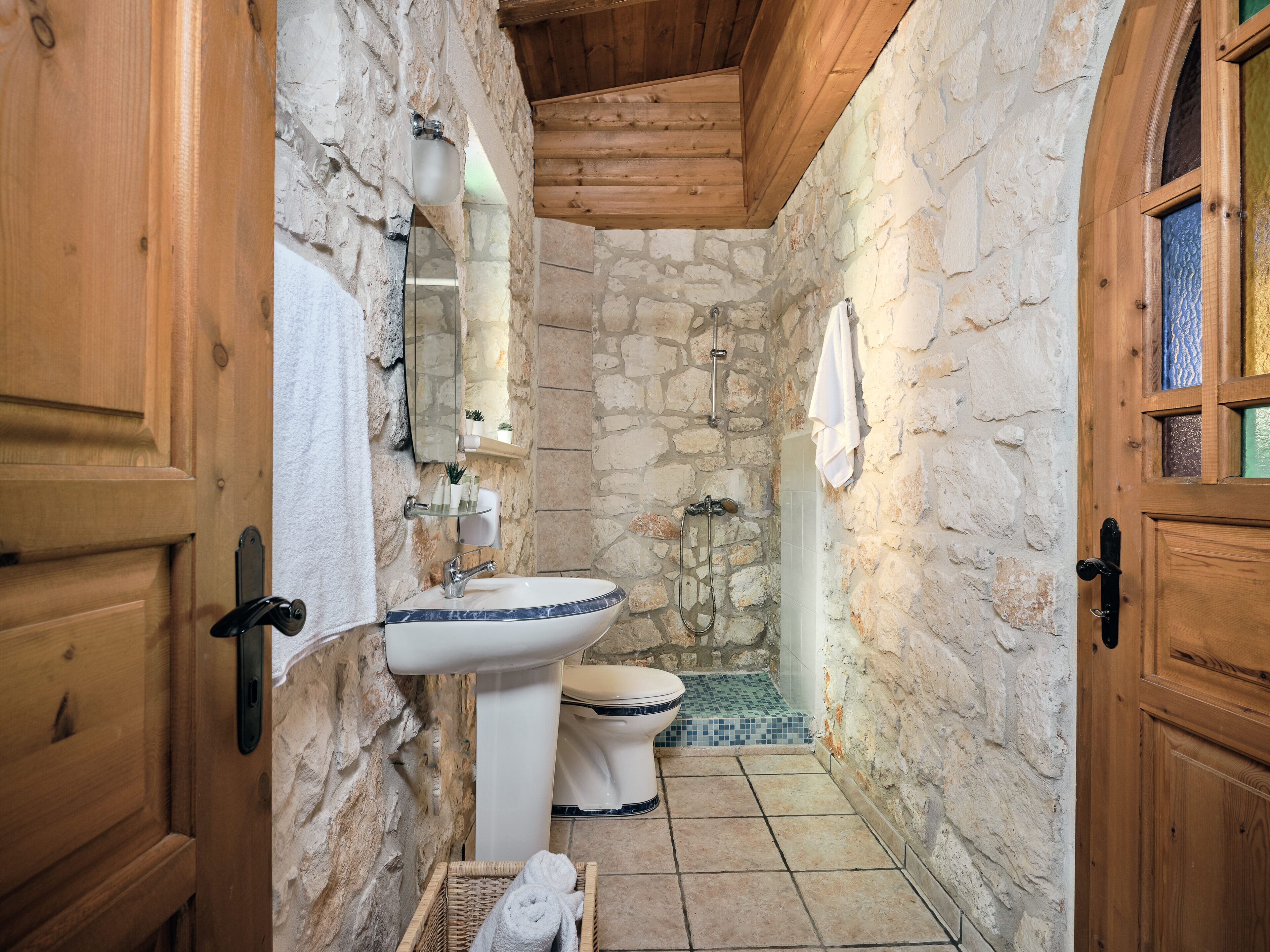 Une salle de bain aux murs en pierre, équipée d’un lavabo, de toilettes et d’une douche.