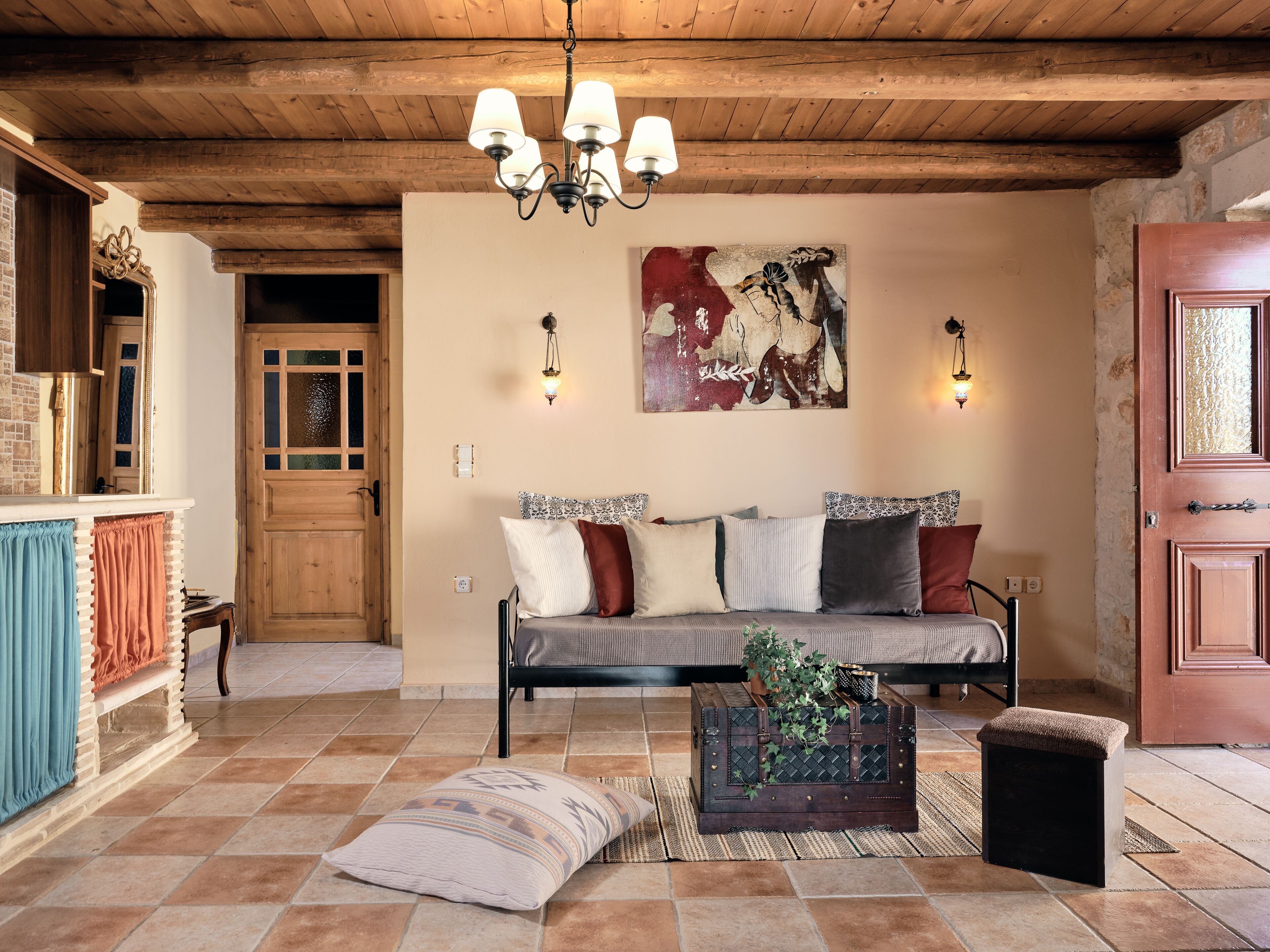 Ein gemütliches Wohnzimmer mit Holzbalkendecke, einer Couch mit gemusterten Kissen, einer Dekorationskiste und einem Bild an der Wand.