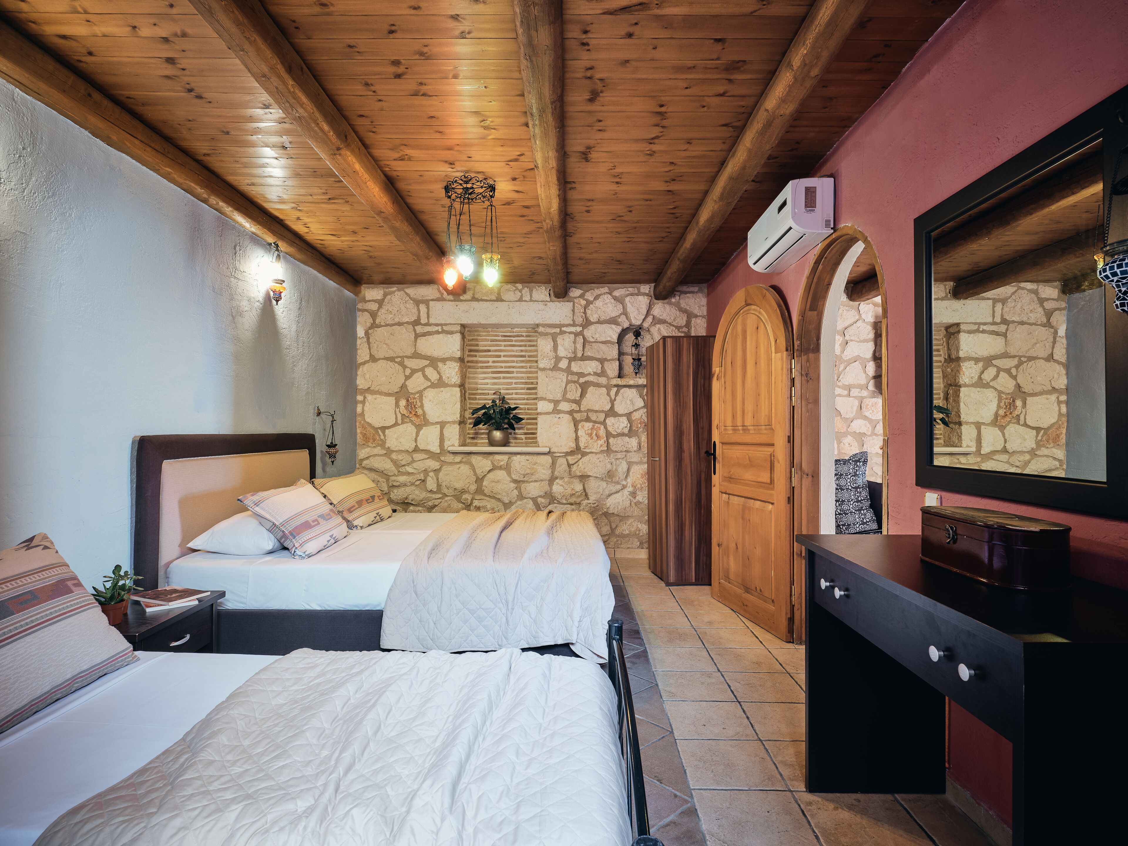 Une chambre avec deux lits, un mur en pierre, des poutres apparentes en bois au plafond, une cheminée en pierre et un grand miroir.