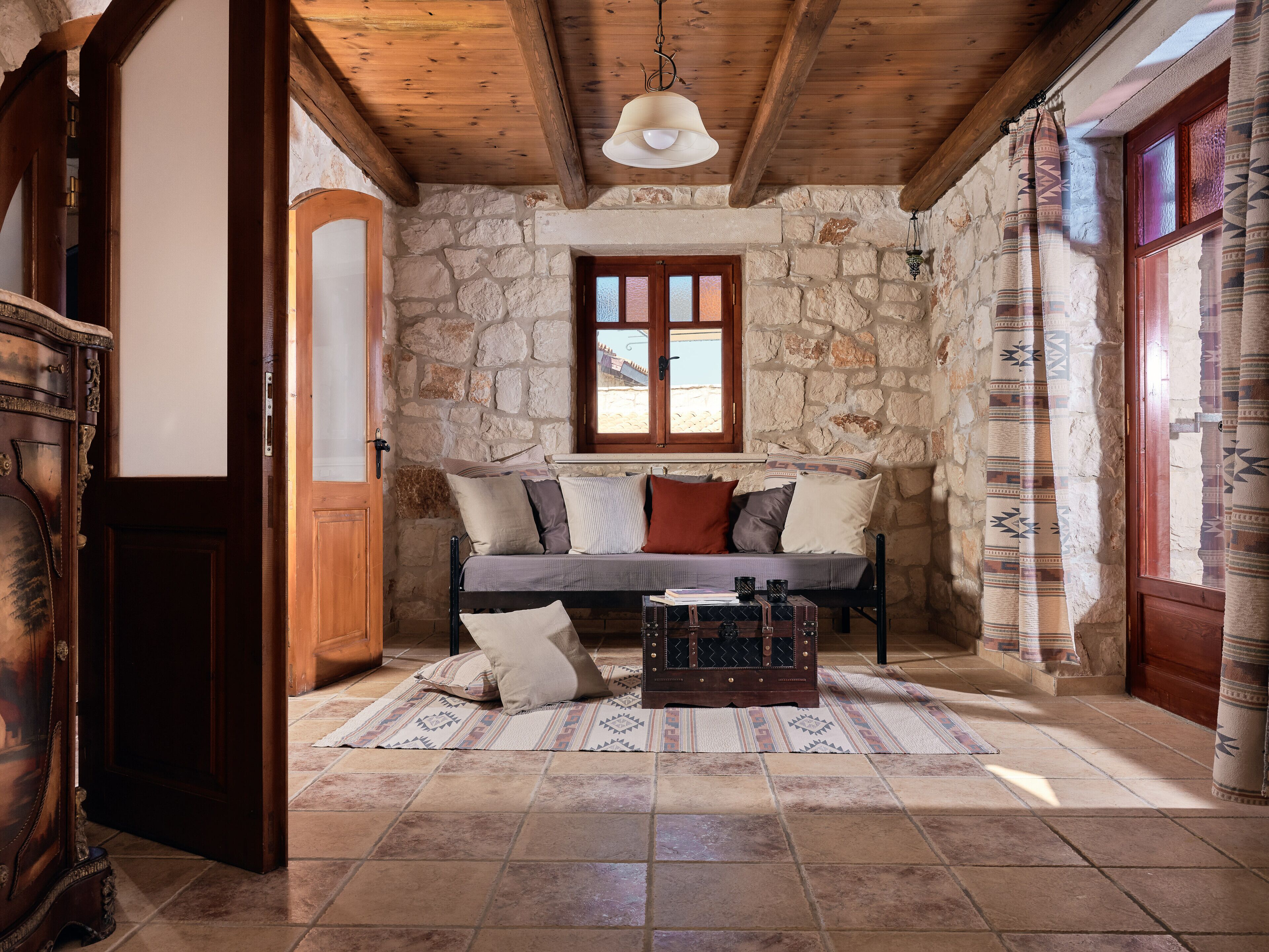 Une pièce chaleureuse avec un mur en pierre, des poutres en bois, un canapé avec des coussins, une table basse et une fenêtre avec des rideaux.