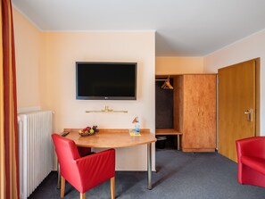 A hotel room with a flat-screen TV mounted on the wall, a wooden table with a fruit bowl, a red chair, and a red sofa. - Hotel Häfner (Bad Schoenborn)