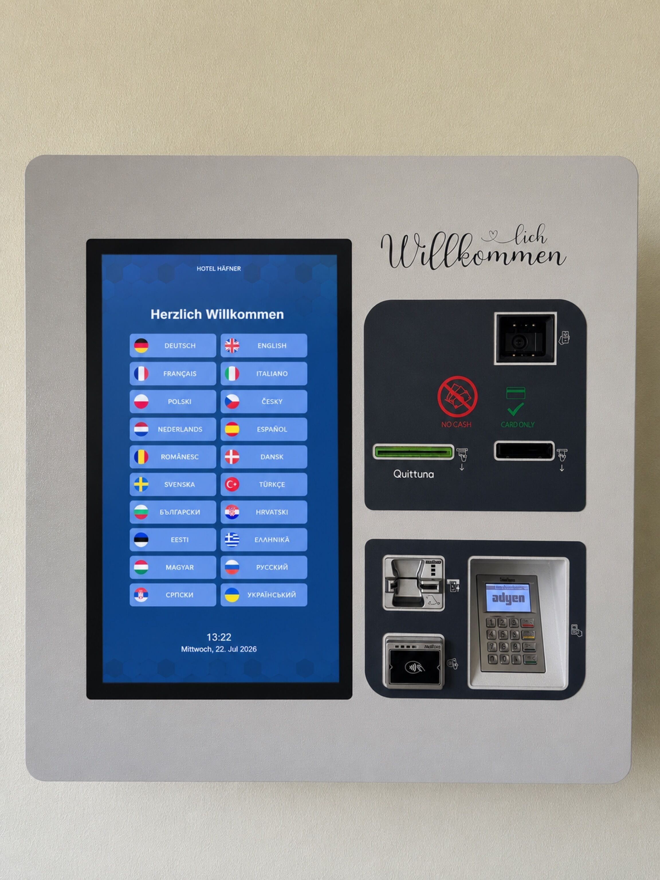 A hotel reception desk with a digital display showing a welcome message in multiple languages, a cashless payment option, and a card reader.