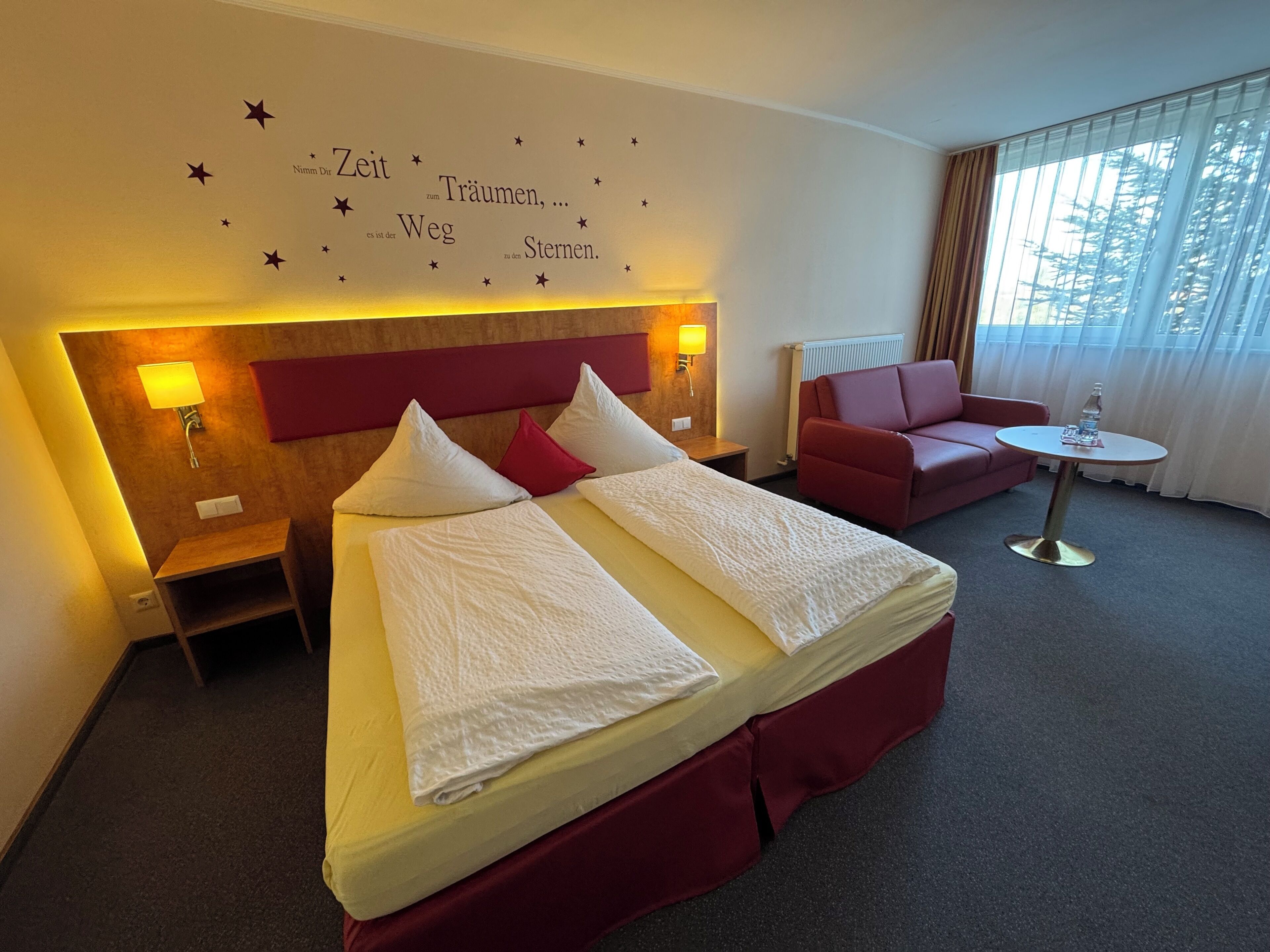 A hotel room with a bed, a red sofa, a small table, and a wall with star decorations.