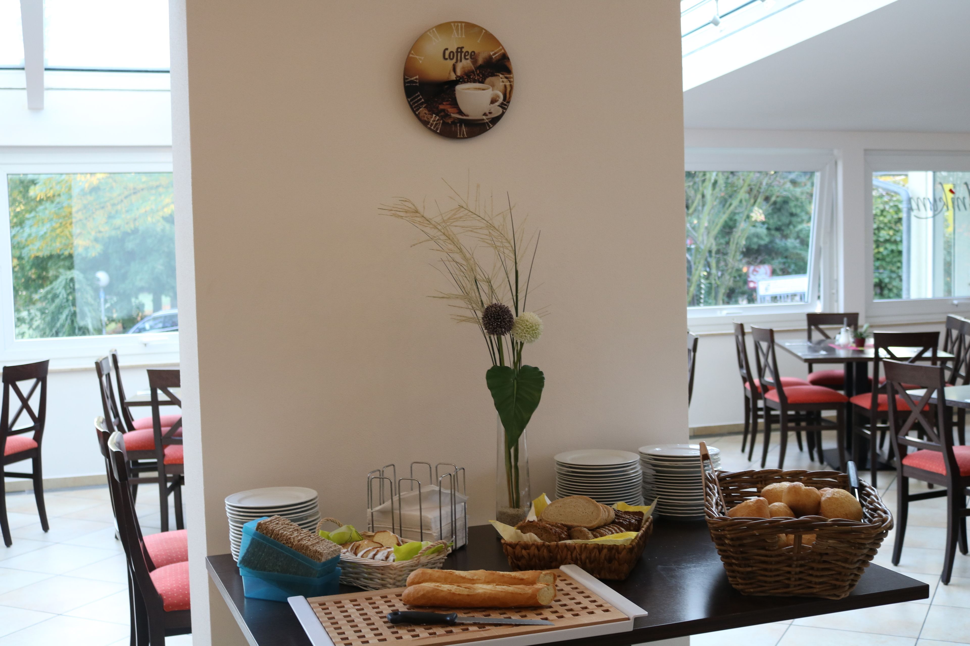 A dining area with a buffet setup, including plates, bread, and a coffee-themed wall clock.