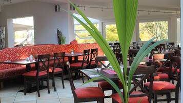Un restaurante con asientos tapizados en rojo y mesas de madera, con una planta verde grande al frente.