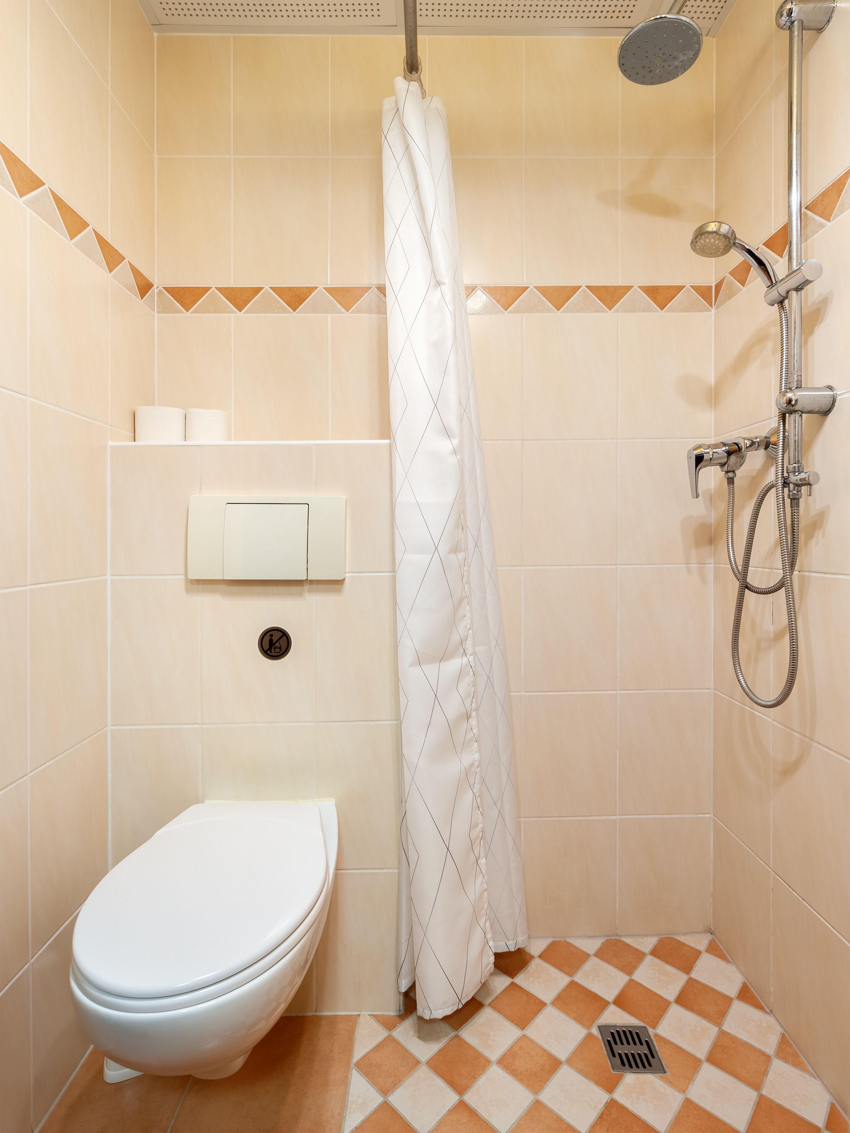 Een kleine betegelde badkamer met toilet, douche met gordijn en een wandmengkraan.