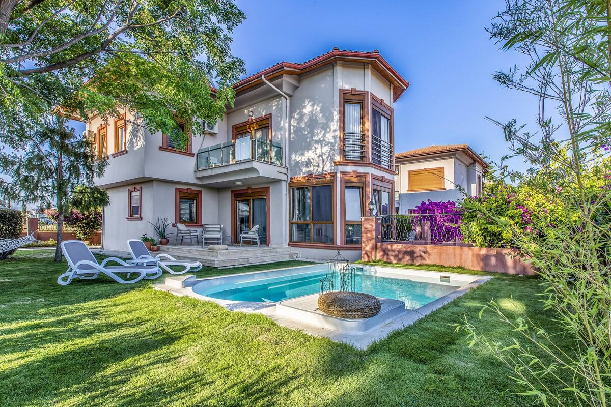 A two-story house with a swimming pool, a balcony, and a well-maintained lawn.