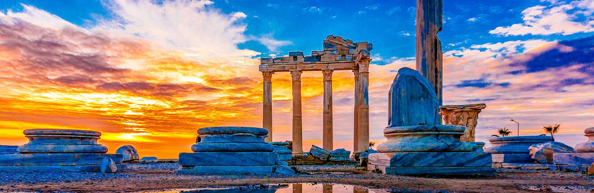 Ruinas antiguas con columnas y estructuras de piedra bajo un cielo al atardecer.