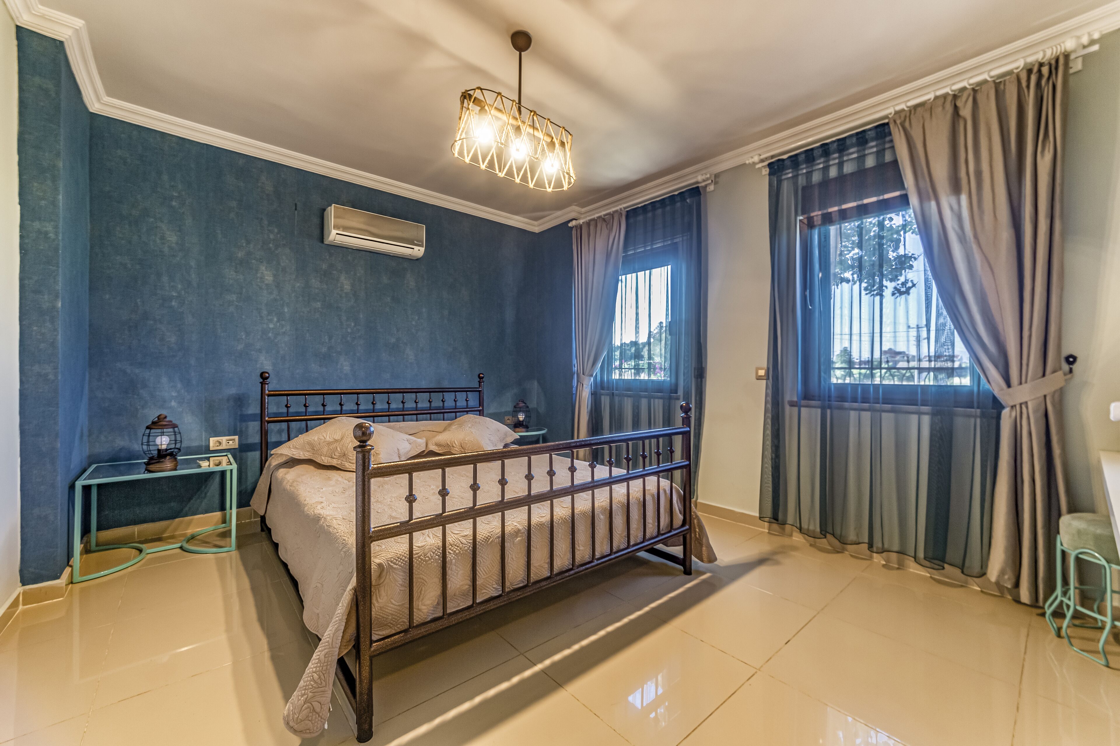 Une chambre à coucher avec un lit, un climatiseur, une table de chevet, une fenêtre avec des rideaux et une vue sur l’extérieur.