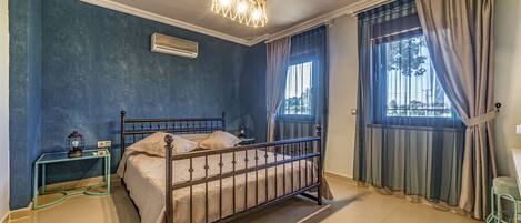 Une chambre à coucher avec un lit, un climatiseur, une table de chevet, une fenêtre avec des rideaux et une vue sur l’extérieur.