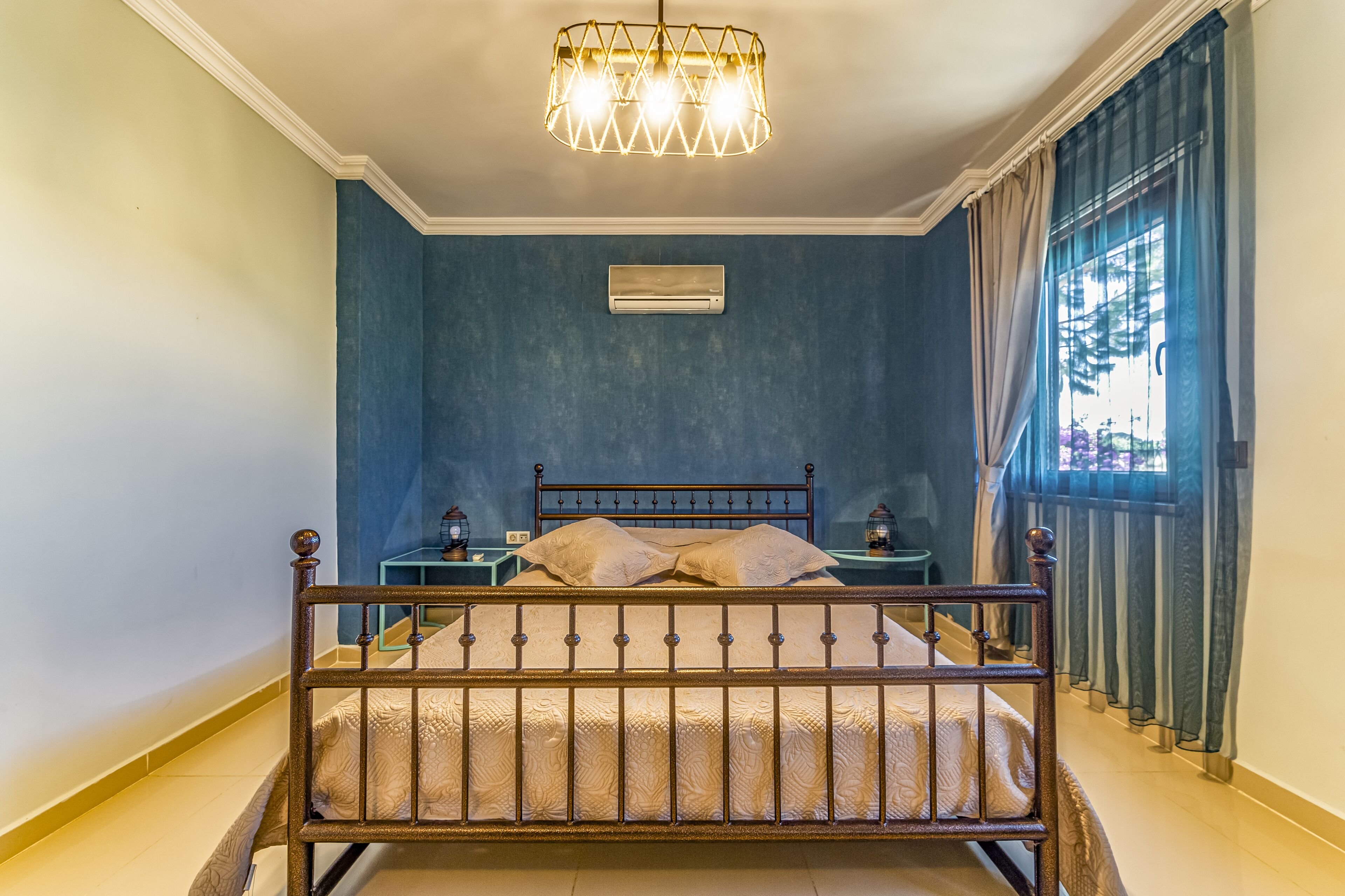 Un dormitorio con cama, mesitas de noche, aire acondicionado y una ventana con cortinas.