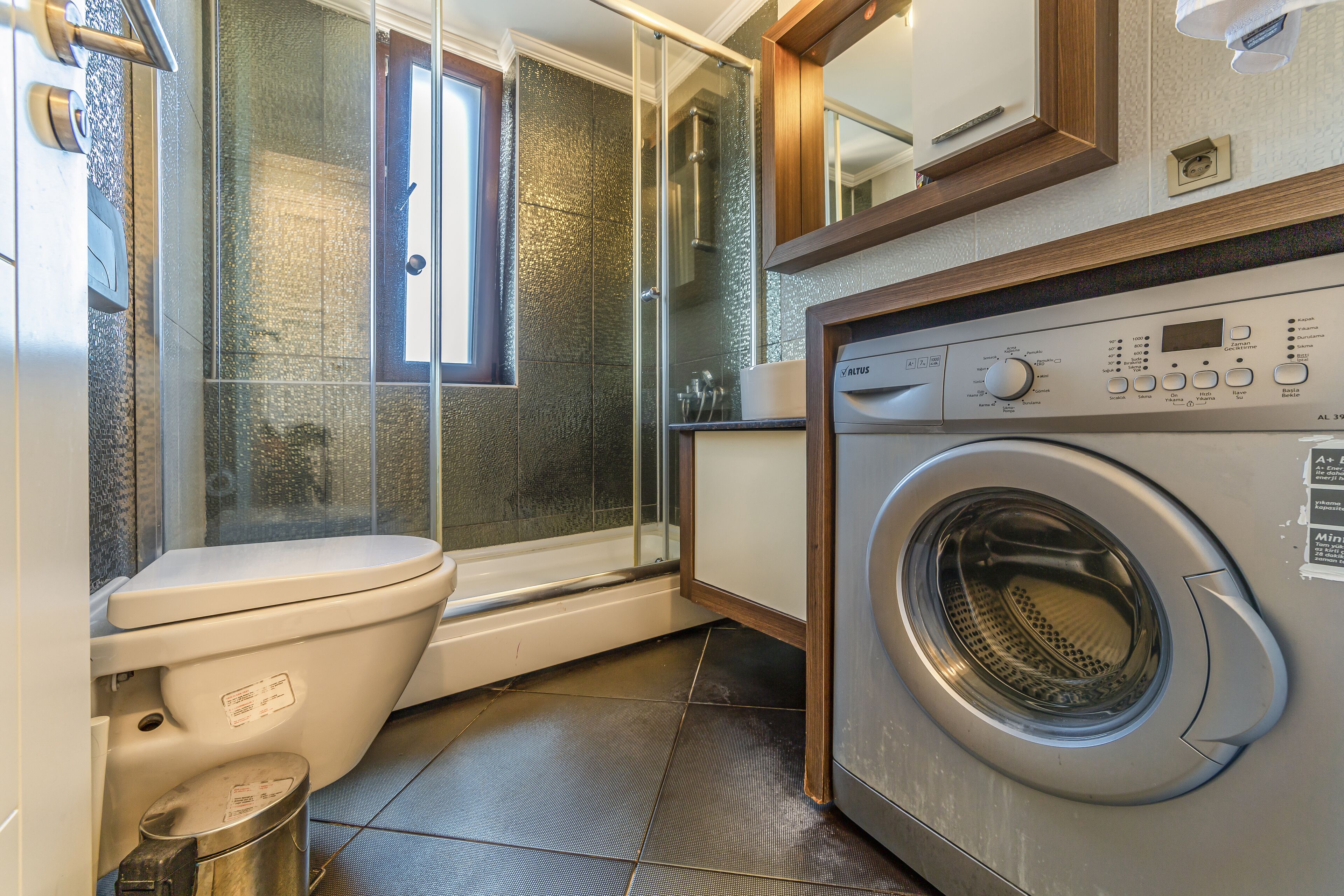 A compact bathroom with a toilet, shower, and washing machine.