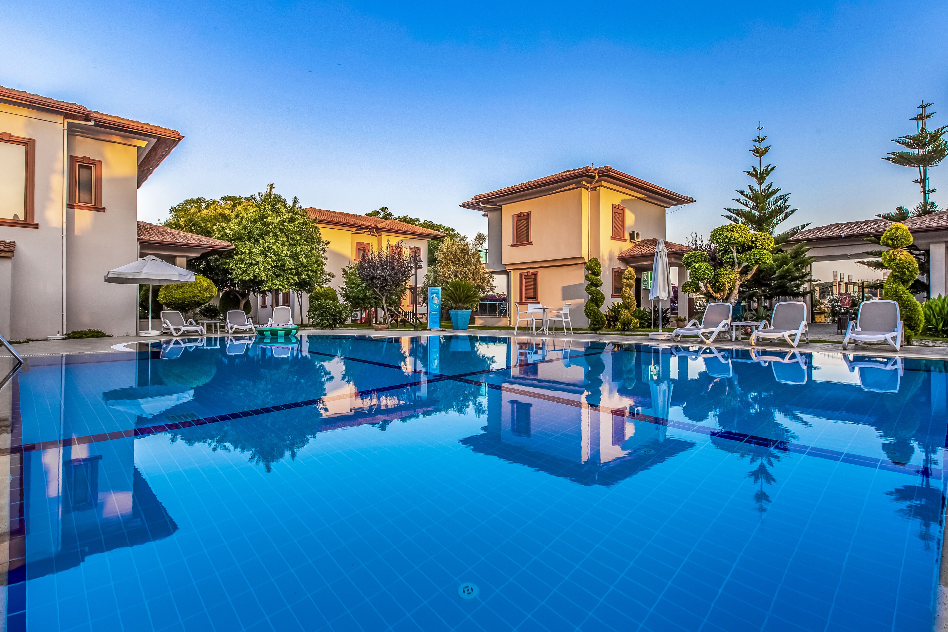 A swimming pool with lounge chairs, surrounded by buildings with tiled roofs and greenery.