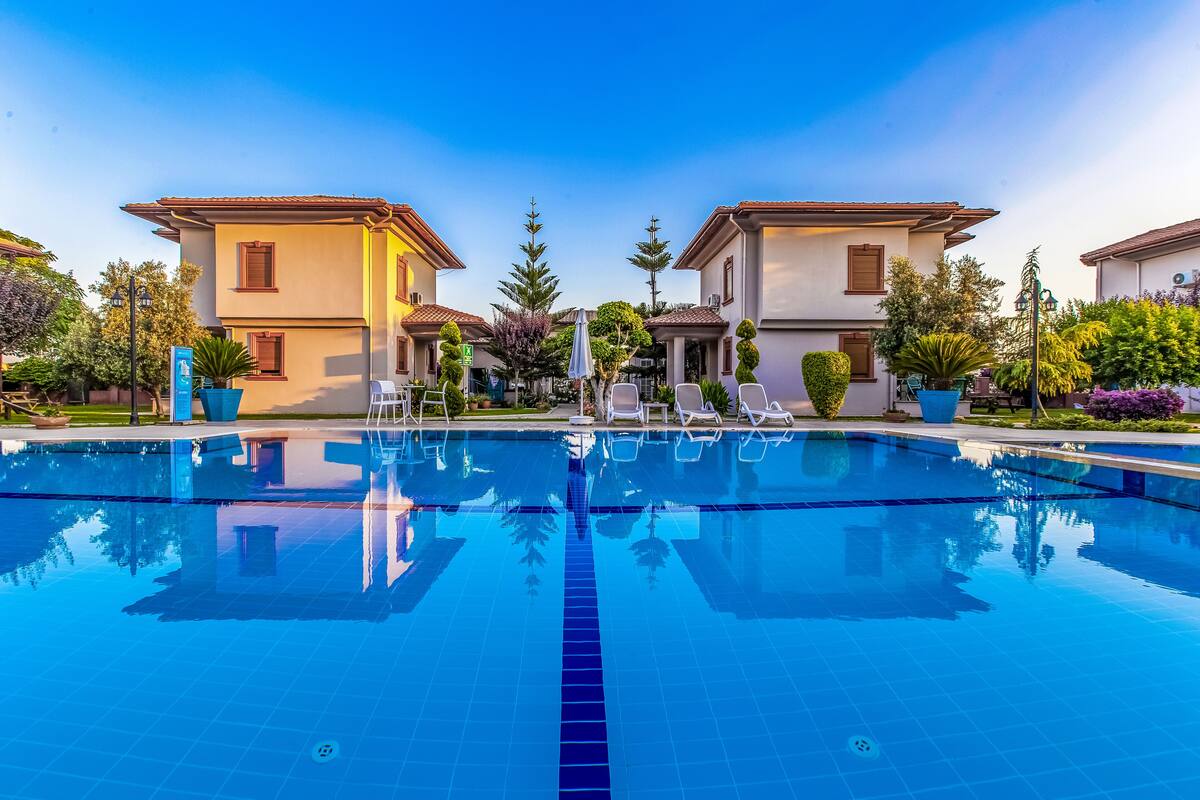 A swimming pool with lounge chairs and potted plants, surrounded by buildings with tiled roofs.
