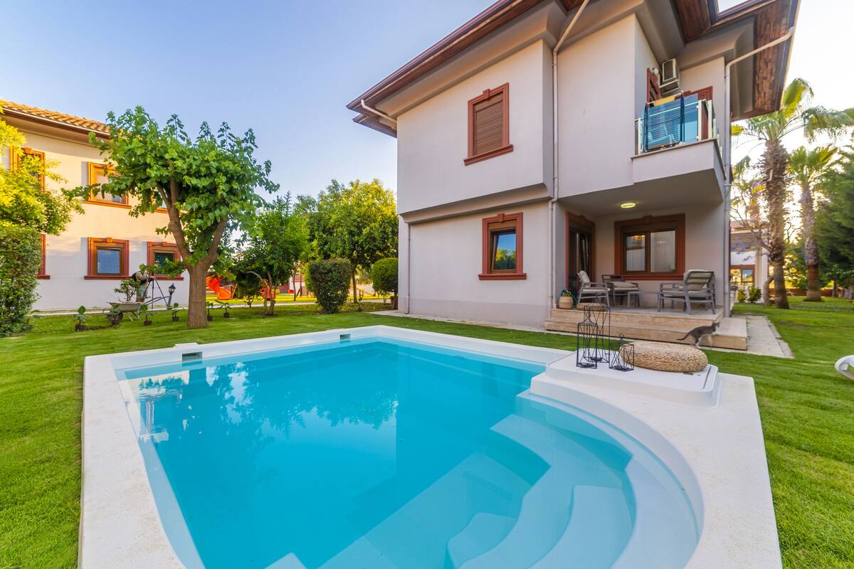 A two-story house with a swimming pool, outdoor furniture, and a well-maintained garden.