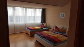 A room with two beds, a window with sheer curtains, a wall-mounted picture, and a wooden floor. - Müritz-Pension Waren (Waren (Müritz))