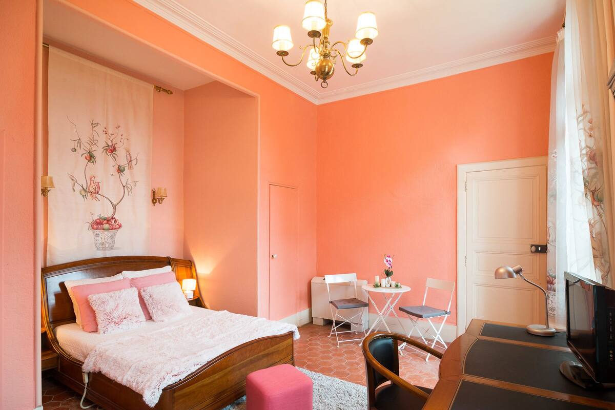 A bedroom with a bed, bedside table, chair, desk, and a television.