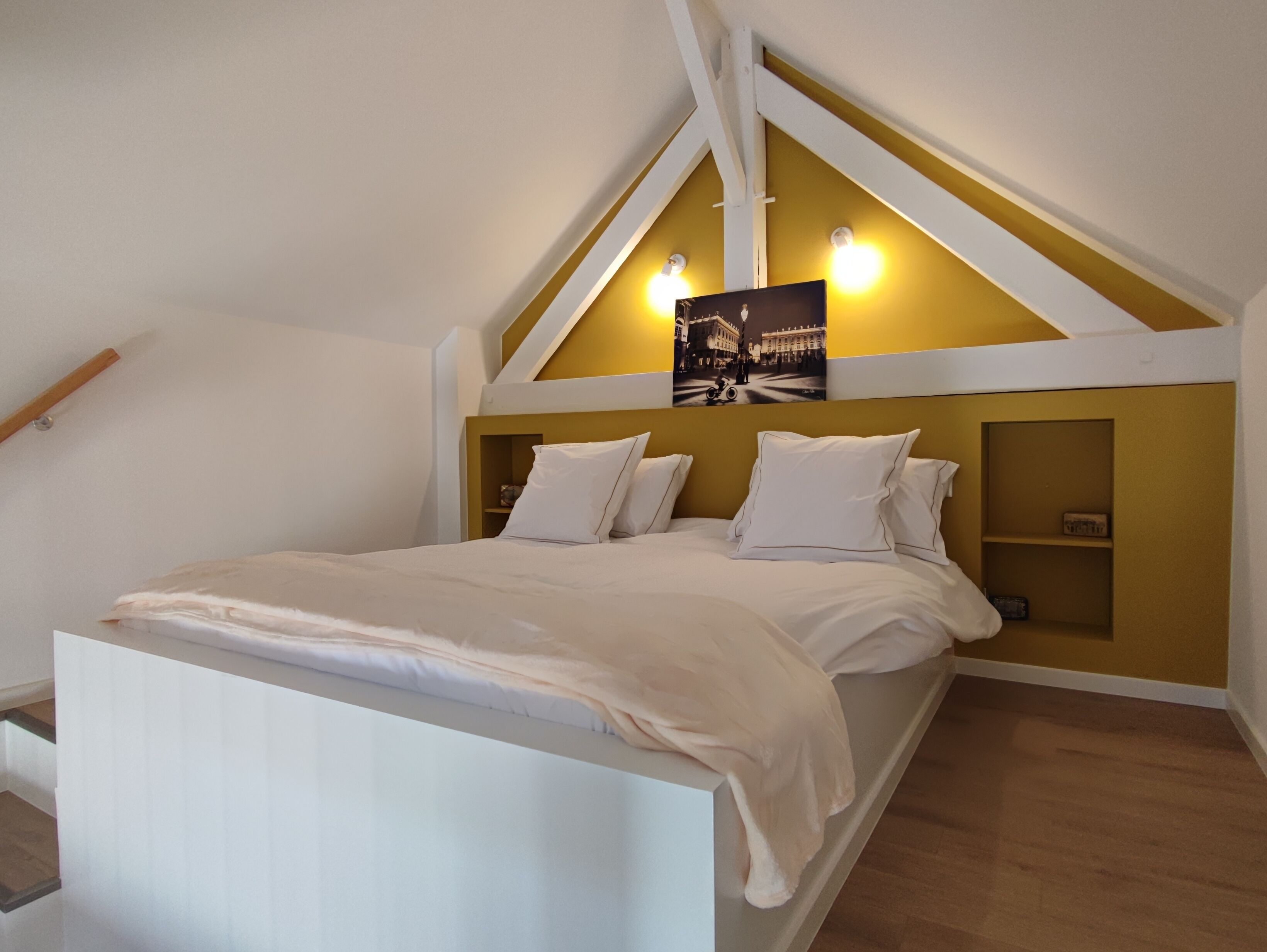 Ein Schlafzimmer mit schrägen Wänden, einem Bett mit weißer Bettwäsche, zwei Nachttischen und einer wandmontierten Lampe.